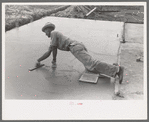 Smoothing concrete floor at migrant camp under construction at Sinton, Texas