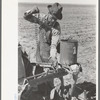 Day laborer putting chain onto feeder gear of planter on farm near Ralls, Texas