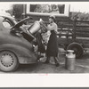 Loading empty milk cans into back of car, creamery, San Angelo, Texas