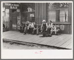 Crowd of men sitting on board walk in front of bar at Mogollon, New Mexico, gold mining town