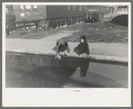 Children playing in water backed up in gutter, South Side of Chicago, Illinois