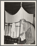 Aged Cajun woman tucking in mosquito bar under mattress. Near Crowley, Louisiana