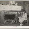 Mrs. Bagget and two children in front of fireplace. Note the board window. Laurel, Mississippi