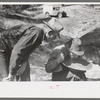 Gold prospector blowing away dirt to find the gold in his pan while a visiting prospector looks on, Pinos Altos, New Mexico