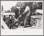Farmer drilling water well. In this picture he is loosening and tightening rope around the pulley, thus raising and lowering the drilling tool, Pie Town, New Mexico
