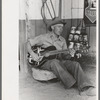 Farm boy playing guitar in front of the filling station and garage, Pie Town, New Mexico