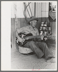 Farm boy playing guitar in front of the filling station and garage, Pie Town, New Mexico