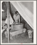 Migrant white mother washing clothes in front of tent home. Weslaco, Texas