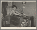 Son of migrant worker reaching for lamp atop cabinet in trailer home. Weslaco, Texas