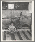 Child of migrant parents sitting on drop bed in trailer home. Weslaco, Texas