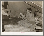 White migrant worker lying on bed in tent home near Mercedes, Texas