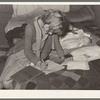 Daughter of migrant auto wrecker doing her lessons on bed in tent home. Corpus Christi, Texas