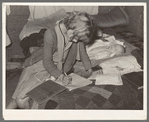 Daughter of migrant auto wrecker doing her lessons on bed in tent home. Corpus Christi, Texas