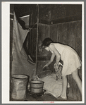 Mexican girl standing over pan of hot coal in which pail of water is heating. Robstown, Texas