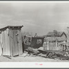 Privy and wrecked automobile in backyard of Mexican home. Old automobile parts are saved for use in construction of fences, sheds and houses. Crystal City, Texas