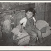 Mexican boy sitting on bedroll. These rolls are used on the floor for beds at night, rolled up during the day. San Antonio, Texas