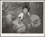 Mexican boy sitting on bedroll. These rolls are used on the floor for beds at night, rolled up during the day. San Antonio, Texas