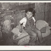 Mexican boy sitting on bedroll. These rolls are used on the floor for beds at night, rolled up during the day. San Antonio, Texas