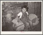Mexican boy sitting on bedroll. These rolls are used on the floor for beds at night, rolled up during the day. San Antonio, Texas