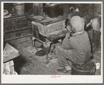 Negro boy sitting by the stove on a cold day in the strawberry picking season. Near Independence, Louisiana