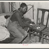 Negro man lighting lamp in bedroom of his home near Hammond, Louisiana. He works for a strawberry grower, doing odd jobs about the place