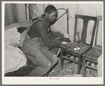 Negro man lighting lamp in bedroom of his home near Hammond, Louisiana. He works for a strawberry grower, doing odd jobs about the place