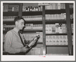 Druggist in front of patent medicine shelf. San Augustine, Texas