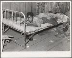 Boy resting on bed in attic of sharecropper shack, New Madrid County, Missouri