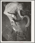 Saddle maker sewing in repairing saddle. Notice awl in his hand. Saddle shop, Alpine, Texas