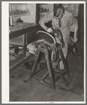 Saddle maker applying cement to glue parts of saddle together. Saddle shop, Alpine, Texas