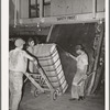 Guiding compressed bale of cotton onto hand truck. Compress, Houston, Texas