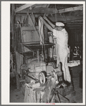 Proprietor of feed mill emptying sack of shelled corn into hopper for grinding into cornmeal. Taylor, Texas