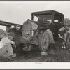 Migrant steeple-jack dropping the pan of his automobile before replacing burned-out bearing. His father and wife are also shown. When he secures a job, the entire family, consisting of his father and mother, wife and sister, all help with the painting