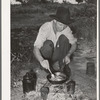 Migrant worker cooking fatback over wood fire in camp near Prague, Oklahoma. Lincoln County