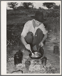 Migrant worker cooking fatback over wood fire in camp near Prague, Oklahoma. Lincoln County