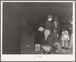 Group of men gathered around remains of fire at early morning vegetable market. San Angelo, Texas