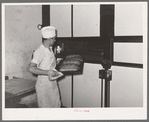 Removing tray of freshly baked bread from conveyor type oven. Bakery, San Angelo, Texas