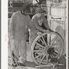 Negro farmer and blacksmith shop workman look over much-repaired wagon wheels to see if they can be made usable again. Depew, Oklahoma