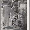 Negro farmer and blacksmith shop workman look over much-repaired wagon wheels to see if they can be made usable again. Depew, Oklahoma