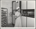 Putting loaves of bread into conveyor type oven for baking. Bakery, San Angelo, Texas