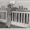 Attendant dumping bucketfull of cattle ration into feed stalls for cows to eat while being milked. Dairy, Tom Green County, Texas