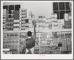 Placing packaged goods on display rack. Retail grocery, San Angelo, Texas