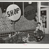 Trucks unload fresh vegetables from early morning market. The clerk takes them in from the sidewalks and arranges them on the display racks. Retail grocery, San Angelo, Texas