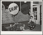 Trucks unload fresh vegetables from early morning market. The clerk takes them in from the sidewalks and arranges them on the display racks. Retail grocery, San Angelo, Texas