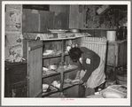 Removing plates from kitchen cupboard in home of Pomp Hall, Negro tenant farmer. Creek County, Oklahoma