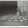 Cowboy shoveling feed into pans for the stock which he is tending while at the San Angelo Fat Stock Show, San Angelo, Texas