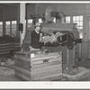 Workman feeding raw wool into machine which removes loose dust and dirt and burs. Wool scouring plant, San Marcos, Texas