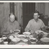 Dinner in the home of a rehabilitation borrower during goat shearing and kidding season. Man on the right is rehabilitation borrower and the one on the left is neighboring rancher who has been hired to help out with this seasonal work