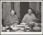 Dinner in the home of a rehabilitation borrower during goat shearing and kidding season. Man on the right is rehabilitation borrower and the one on the left is neighboring rancher who has been hired to help out with this seasonal work