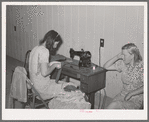 Wife of migratory agricultural laborer sewing at the Aqua Fria migratory labor camp, Arizona. These machines are rented for a nominal sum which remains in the camp fund to be used as the camp committee decides